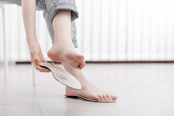 Mujer ajustando plantilla ortopédica en el interior, de cerca. Chica sosteniendo una plantilla junto a un pie en casa. Plantillas ortopédicas. Banner de cuidado del pie. Corrección de pies planos. Tratamiento y prevención de enfermedades del pie — Foto de Stock