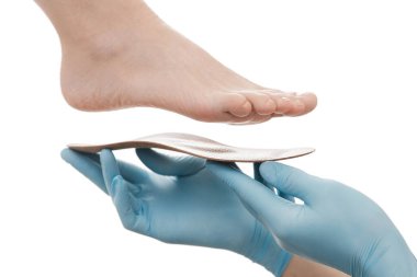 Ortopedik insole beyaz bir arkaplanda izole edildi. Lastik eldivenli eller ortopedik tabanı tutuyor. Ayak bakımı, ayaklara iyi gelir. Doktor ortopedist tıbbi cihazı test ediyor. Düz taban düzeltmesi