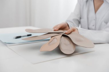 Doktor masada otururken taban tabanı tutuyor. Ortopedist tıbbi cihazı test ediyor. Ortopedik tabanlar. Ayak bakımı. Düz Ayak Düzeltme. Düztaban ve ayak hastalıklarının tedavisi ve önlenmesi