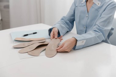 Doktor masada otururken taban tabanı tutuyor. Ortopedist tıbbi cihazı test ediyor. Ortopedik tabanlar. Ayak bakımı. Düz Ayak Düzeltme. Düztaban ve ayak hastalıklarının tedavisi ve önlenmesi