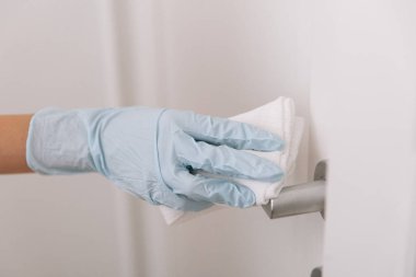 Siyah kapı kollarını antiseptik ıslak mendille mavi eldivenlerle temizliyorum. Hastane ve kamusal alanlarda korona virüsüne karşı korunma yüzeylerini sterilize edin. Kadın eli temizlik için havlu kullanıyor.