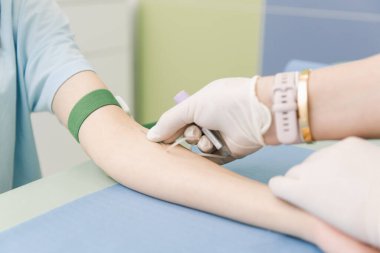 Tedavi odasındaki bir damardan kan testi alıyorum. Hemşire şırıngayı hastanın eline iğneyle batırıyor. Kan bağışı sırasında enjeksiyon yerine baskı yapılmış. Kanlı tüp