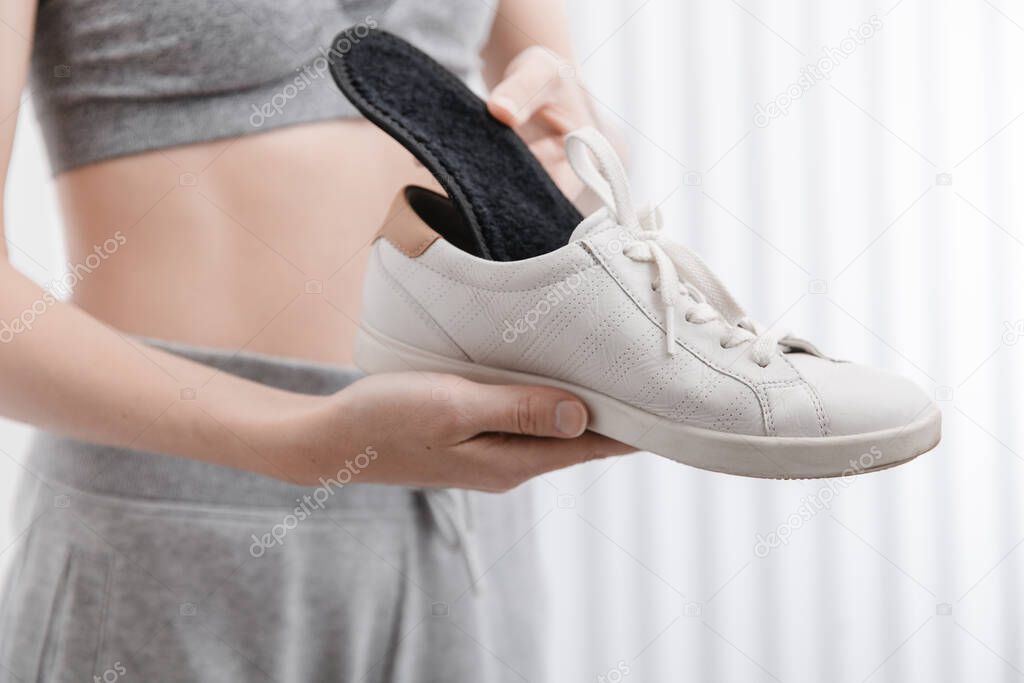 Woman putting orthopedic insole into shoe at home. Sports girl fitting orthopedic insole indoors, close up. Foot care banner. Flat Feet Correction. Treatment and prevention of foot diseases