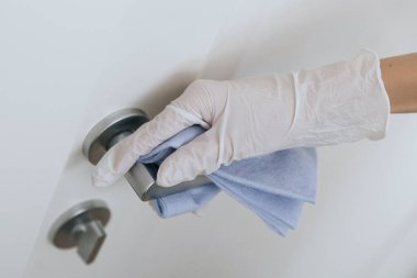 Beyaz eldivenli, mavi mendilli kapı kolu. Ev kapısı bağlantısını temizlemek için havlu kullanan kadın eli. Hastane ve halka açık alanlarda korona virüsüne karşı yüzeylerin sterilize edilmesi.