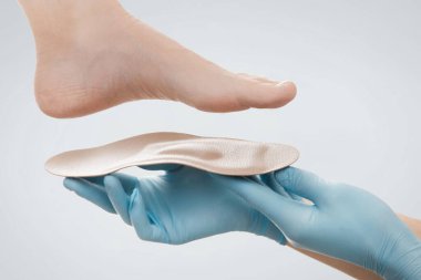 Ortopedik insole beyaz bir arkaplanda izole edildi. Lastik eldivenli eller ortopedik tabanı tutuyor. Ayak bakımı, ayaklara iyi gelir. Doktor ortopedist tıbbi cihazı test ediyor. Düz taban düzeltmesi