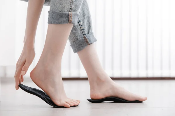 Kadın ortopedik insole 'u içeride takıyor, kapatın. Evde ayağının yanında taban tutan bir kız. Ortopedik tabanlar. Ayak bakımı afişi. Düz Ayak Düzeltme. Ayak hastalıklarının tedavisi ve önlenmesi