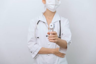 Sıcaklık ölçüm silahı doktorun elinde. Doktorun koruyucu cerrahi maske takıp vücut ısısını kontrol etmek için kızılötesi izometrik termometre tabancası kullanmaya hazır olduğu yakın çekim.
