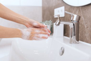 Akan su musluğunun altında ellerini yıkamak. Corona virüsünün önlenmesi için sabunla ellerini ovuşturmak, korona virüsü bulaştırmamak için hijyen. Ya da umumi tuvalette. Hijyen konsepti el detayı