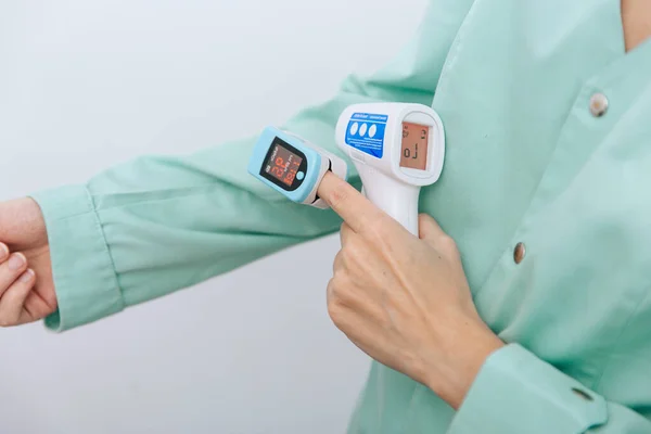 Όπλο μέτρησης θερμοκρασίας σε χέρια γιατρού. Κοντινό πλάνο του γιατρού φορώντας προστατευτική χειρουργική μάσκα έτοιμη να χρησιμοποιήσει υπέρυθρο ισομετρικό όπλο θερμόμετρο για να ελέγξει τη θερμοκρασία του σώματος για συμπτώματα του ιού — Φωτογραφία Αρχείου