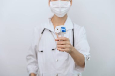 Sıcaklık ölçüm silahı doktorun elinde. Doktorun koruyucu cerrahi maske takıp vücut ısısını kontrol etmek için kızılötesi izometrik termometre tabancası kullanmaya hazır olduğu yakın çekim.