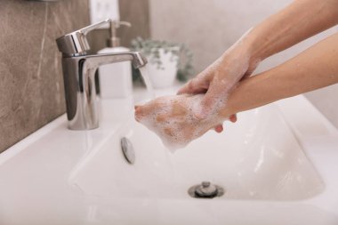 Akan su musluğunun altında ellerini yıkamak. Corona virüsünün önlenmesi için sabunla ellerini ovuşturmak, korona virüsü bulaştırmamak için hijyen. Ya da umumi tuvalette. Hijyen konsepti el detayı
