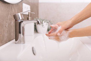 Akan su musluğunun altında ellerini yıkamak. Corona virüsünün önlenmesi için sabunla ellerini ovuşturmak, korona virüsü bulaştırmamak için hijyen. Ya da umumi tuvalette. Hijyen konsepti el detayı