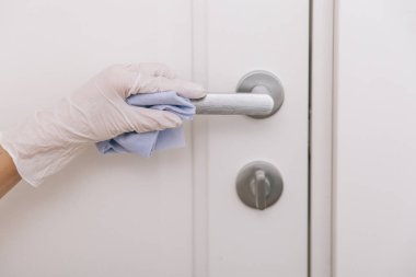 Beyaz eldivenli, mavi mendilli kapı kolu. Ev kapısı bağlantısını temizlemek için havlu kullanan kadın eli. Hastane ve halka açık alanlarda korona virüsüne karşı yüzeylerin sterilize edilmesi.