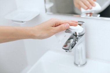 Lavabo musluğunu mikrofiber bezle temizliyorum. Banyoyu temizliyorum. Hastane ve kamusal alanlarda korona virüsüne karşı korunma yüzeylerini sterilize edin. Islak mendil kullanan kadın eli