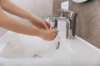 Akan su musluğunun altında ellerini yıkamak. Corona virüsünün önlenmesi için sabunla ellerini ovuşturmak, korona virüsü bulaştırmamak için hijyen. Ya da umumi tuvalette. Hijyen konsepti el detayı