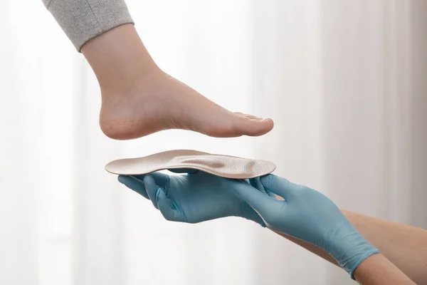 Beyaz arka planda ortopedik taban. Lastik eldivenli eller ortopedik tabanı tutuyor. Ayak bakımı, ayaklara iyi gelir. Doktor ortopedist tıbbi cihazı test ediyor. Düz taban düzeltmesi