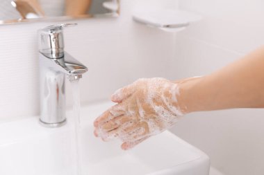 Akan su musluğunun altında ellerini yıkamak. Corona virüsünün önlenmesi için sabunla ellerini ovuşturmak, korona virüsü bulaştırmamak için hijyen. Ya da umumi tuvalette. Hijyen konsepti el detayı