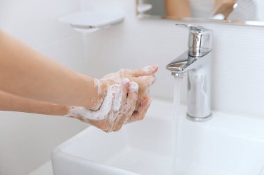 Akan su musluğunun altında ellerini yıkamak. Corona virüsünün önlenmesi için sabunla ellerini ovuşturmak, korona virüsü bulaştırmamak için hijyen. Ya da umumi tuvalette. Hijyen konsepti el detayı