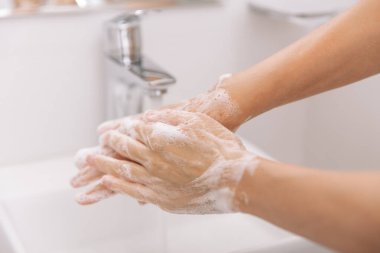 Akan su musluğunun altında ellerini yıkamak. Corona virüsünün önlenmesi için sabunla ellerini ovuşturmak, korona virüsü bulaştırmamak için hijyen. Ya da umumi tuvalette. Hijyen konsepti el detayı
