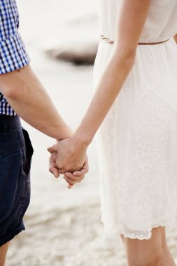 Deniz kıyısında el ele tutuşan sevimli bir çift. Aşk hikayesi ya da sevgililer günü konsepti. Tatil ya da balayı için genç bir erkek ve kadının siluetleri. Sonsuza dek aşk bayrağı ya da kartpostal.