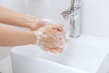 Akan su musluğunun altında ellerini yıkamak. Corona virüsünün önlenmesi için sabunla ellerini ovuşturmak, korona virüsü bulaştırmamak için hijyen. Ya da umumi tuvalette. Hijyen konsepti el detayı.