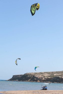Profesyonel uçurtma sörfçüleri gün batımında deniz suyuyla birlikte bir gölün üzerinde tahtayla sörf yaparlar. Su sıçrıyor ve güneş parlıyor. Su sporları. Birçok insanın panoramik görüntüsü uçurtma sörfü tahtası sürmekten zevk alır.