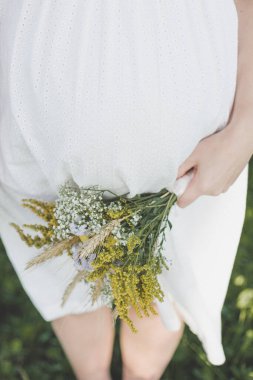 Hamilelik, annelik, insanlar ve beklenti konsepti. Doğada koca göbekli hamile bir kadının yakın çekimi. Beyaz elbiseli hamile bir kadın çocuk bekliyor. Kartpostal, afiş