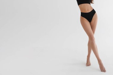Beyaz stüdyo arka planında bronzlaşmış ince bacaklı bir kadın. Spor kıyafetleriyle fitness modeline yakın çekim. İç çamaşırı ya da iç çamaşırı reklamı. Cilt bakımı veya diyet pankartı.