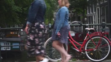 Amsterdam 'da bir kanalda eski kırmızı bir bisiklet. Oradan insanlar ve bisikletler geçiyor.