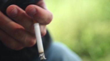 Parkta yanan bir sigara tutan bir adamın eline yaklaş.