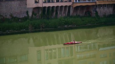Güneşli bir yaz gününde Arno nehrinde tek başına kürek çeken bir adam Floransa şehir merkezinde.