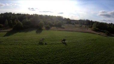 Bir FPV 'nin üzerinde at sırtında uçarken, at üstünde bir kız, yeşil bir tarlada, ormanın arka planında, çalılarda, ağaçlarda, mavi gökyüzünde, beyaz bulutlarda