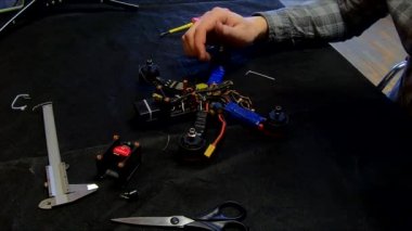 Parçalanmış FPV kuadrokopteri, siyah bir masanın üzerine kendin yap drone onarımı, eski plastik bir çerçevenin çıkarılması, kırık parçalar, İngiliz anahtarı ve tornavida ile sökülmesi, elektronik, mikro devreler, tamir, lehimleme.