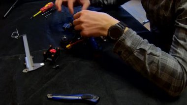 Parçalanmış FPV kuadrokopteri, siyah bir masanın üzerine kendin yap drone onarımı, eski plastik bir çerçevenin çıkarılması, kırık parçalar, İngiliz anahtarı ve tornavida ile sökülmesi, elektronik, mikro devreler, tamir, lehimleme.