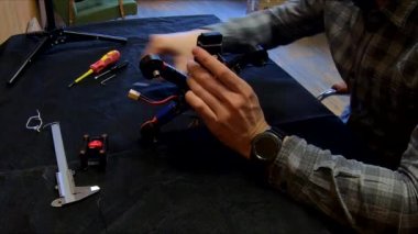 Parçalanmış FPV kuadrokopteri, siyah bir masanın üzerine kendin yap drone onarımı, eski plastik bir çerçevenin çıkarılması, kırık parçalar, İngiliz anahtarı ve tornavida ile sökülmesi, elektronik, mikro devreler, tamir, lehimleme.