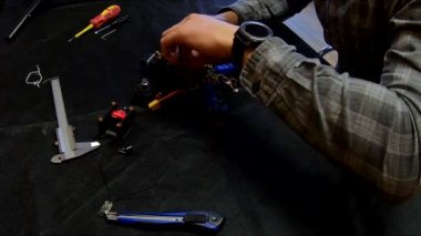 Parçalanmış FPV kuadrokopteri, siyah bir masanın üzerine kendin yap drone onarımı, eski plastik bir çerçevenin çıkarılması, kırık parçalar, İngiliz anahtarı ve tornavida ile sökülmesi, elektronik, mikro devreler, tamir, lehimleme.