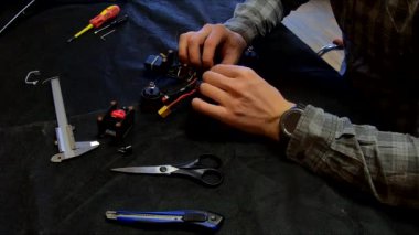 Parçalanmış FPV kuadrokopteri, siyah bir masanın üzerine kendin yap drone onarımı, eski plastik bir çerçevenin çıkarılması, kırık parçalar, İngiliz anahtarı ve tornavida ile sökülmesi, elektronik, mikro devreler, tamir, lehimleme.