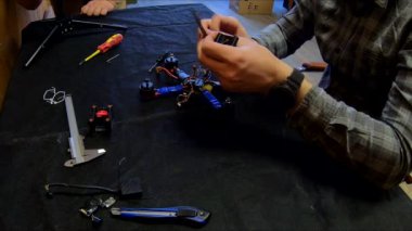Parçalanmış FPV kuadrokopteri, siyah bir masanın üzerine kendin yap drone onarımı, eski plastik bir çerçevenin çıkarılması, kırık parçalar, İngiliz anahtarı ve tornavida ile sökülmesi, elektronik, mikro devreler, tamir, lehimleme.