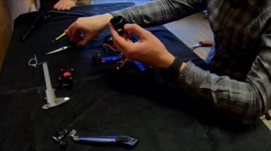 Parçalanmış FPV kuadrokopteri, siyah bir masanın üzerine kendin yap drone onarımı, eski plastik bir çerçevenin çıkarılması, kırık parçalar, İngiliz anahtarı ve tornavida ile sökülmesi, elektronik, mikro devreler, tamir, lehimleme.