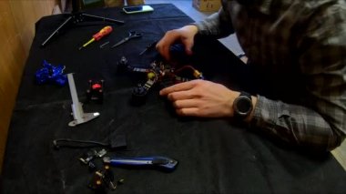 Parçalanmış FPV kuadrokopteri, siyah bir masanın üzerine kendin yap drone onarımı, eski plastik bir çerçevenin çıkarılması, kırık parçalar, İngiliz anahtarı ve tornavida ile sökülmesi, elektronik, mikro devreler, tamir, lehimleme.
