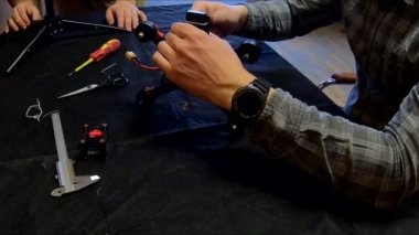 Parçalanmış FPV kuadrokopteri, siyah bir masanın üzerine kendin yap drone onarımı, eski plastik bir çerçevenin çıkarılması, kırık parçalar, İngiliz anahtarı ve tornavida ile sökülmesi, elektronik, mikro devreler, tamir, lehimleme.