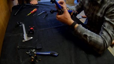 Parçalanmış FPV kuadrokopteri, siyah bir masanın üzerine kendin yap drone onarımı, eski plastik bir çerçevenin çıkarılması, kırık parçalar, İngiliz anahtarı ve tornavida ile sökülmesi, elektronik, mikro devreler, tamir, lehimleme.