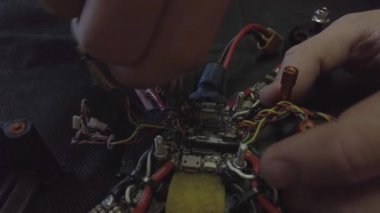 Parçalanmış FPV kuadrokopteri, siyah bir masanın üzerine kendin yap drone onarımı, eski plastik bir çerçevenin çıkarılması, kırık parçalar, İngiliz anahtarı ve tornavida ile sökülmesi, elektronik, mikro devreler, tamir, lehimleme.