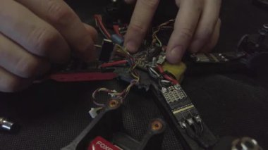 Parçalanmış FPV kuadrokopteri, siyah bir masanın üzerine kendin yap drone onarımı, eski plastik bir çerçevenin çıkarılması, kırık parçalar, İngiliz anahtarı ve tornavida ile sökülmesi, elektronik, mikro devreler, tamir, lehimleme.