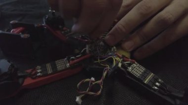 Parçalanmış FPV kuadrokopteri, siyah bir masanın üzerine kendin yap drone onarımı, eski plastik bir çerçevenin çıkarılması, kırık parçalar, İngiliz anahtarı ve tornavida ile sökülmesi, elektronik, mikro devreler, tamir, lehimleme.