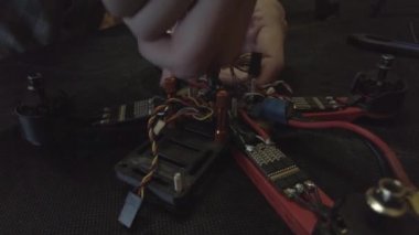 Parçalanmış FPV kuadrokopteri, siyah bir masanın üzerine kendin yap drone onarımı, eski plastik bir çerçevenin çıkarılması, kırık parçalar, İngiliz anahtarı ve tornavida ile sökülmesi, elektronik, mikro devreler, tamir, lehimleme.