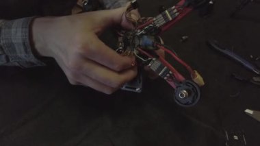Parçalanmış FPV kuadrokopteri, siyah bir masanın üzerine kendin yap drone onarımı, eski plastik bir çerçevenin çıkarılması, kırık parçalar, İngiliz anahtarı ve tornavida ile sökülmesi, elektronik, mikro devreler, tamir, lehimleme.