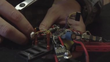 Parçalanmış FPV kuadrokopteri, siyah bir masanın üzerine kendin yap drone onarımı, eski plastik bir çerçevenin çıkarılması, kırık parçalar, İngiliz anahtarı ve tornavida ile sökülmesi, elektronik, mikro devreler, tamir, lehimleme.
