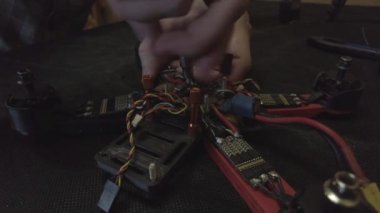 Parçalanmış FPV kuadrokopteri, siyah bir masanın üzerine kendin yap drone onarımı, eski plastik bir çerçevenin çıkarılması, kırık parçalar, İngiliz anahtarı ve tornavida ile sökülmesi, elektronik, mikro devreler, tamir, lehimleme.