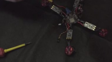 Parçalanmış FPV kuadrokopteri, siyah bir masanın üzerine kendin yap drone onarımı, eski plastik bir çerçevenin çıkarılması, kırık parçalar, İngiliz anahtarı ve tornavida ile sökülmesi, elektronik, mikro devreler, tamir, lehimleme.